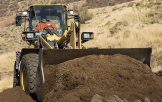 Construction worker operating a front-end loader moving soil at a job site in a dry hillside landscape.