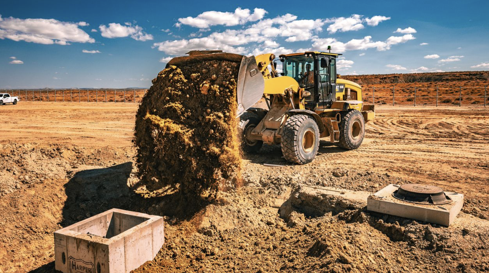 Wheel loader dumping soil into trench at a construction site during site preparation work.